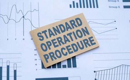 The image shows a cardboard box with the text Standard operation procedure on a background of financial charts and graphs. The concept of the image is business and finance.の写真素材