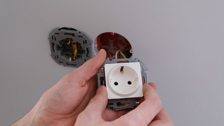 Professional electrician working on a home electrical system, he is installing a wall socket