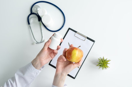 Nutritionist holds an apple and a jar of vitamins in his hands, top view, medical conceptの写真素材