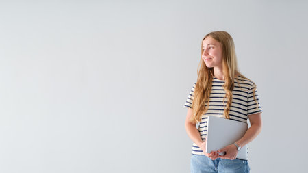 Confident professional woman looking away while standing on a standing wall in casual clothes. Young business woman holding a notepad, ready to start a productive day. Copy Spaceの写真素材