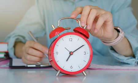 Female hand turning off red alarm clock at workplace closeupの写真素材