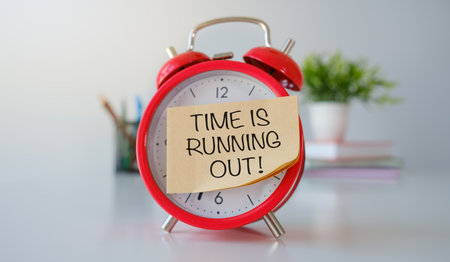 Time is Running Out Text on sticker sworn on red alarm clock on office desk
