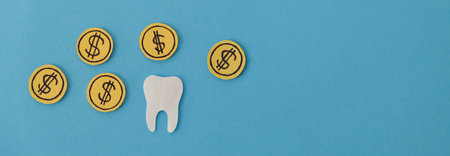 Dental expenses concept: coins surrounding tooth on bright blue background, copy spaceの写真素材
