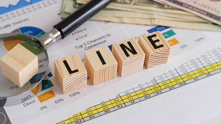 A wooden block with the letters L, I, N, E, and a magnifying glass on top of a piece of paper with charts and numbersの写真素材