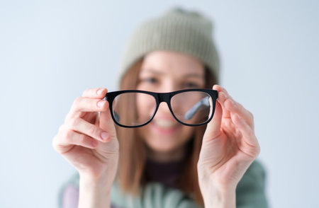 A woman is holding a pair of glasses and smiling. Concept of confidence and positivity, as the woman is proud of her glasses and is happy to show them offの写真素材