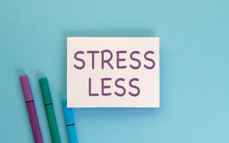 Stress Less is written on a white card. The card is sitting on a blue background. There are three markers on the background, one of which is purpleの写真素材