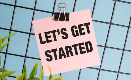 A clip holds a pink piece of paper that says Let's get started. The paper is hanging from a metal frameの写真素材