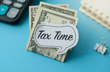 Sticker with text Tax Time with lettering on money banknotes with calculator and notepad on blue...