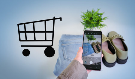A person is holding a cell phone up to a picture of a shopping cart. Concept of shopping and the...