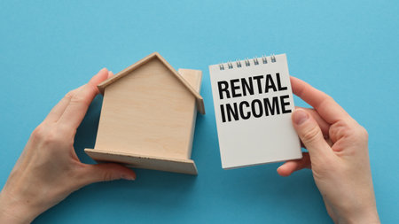 A person holding a house and a notebook with the word Rental Income written on itの写真素材
