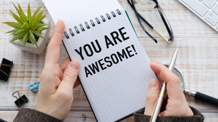 A person is holding a notebook and pen and writing the words You are awesome on itの写真素材
