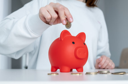 A woman is putting coins into a red piggy bank. Concept of saving money and being financially...