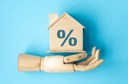 A wooden hand holding a house with a blue background. The house is marked with a percentage signの写真素材