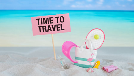 A beach scene with a pink sign that says Time to Travel. The sign is on a stick and is surrounded by...