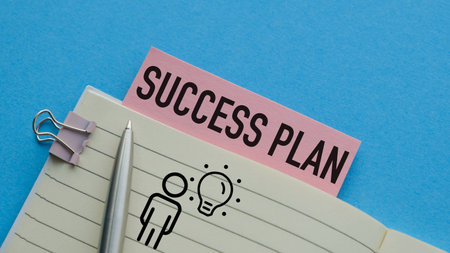 A pen is on a notebook with a pink label that says Success Plan. The notebook is open to a page with...