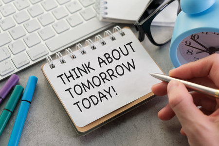 A person is writing on a piece of paper that says Think about tomorrow today. The person is using a pen to write on the paperの写真素材