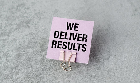 A pink card with the words We Deliver Results written on it. The card is held up by a paper clipの写真素材
