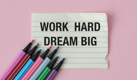 A piece of paper with the words Work Hard Dream Big written on it. The paper is placed on a pink...