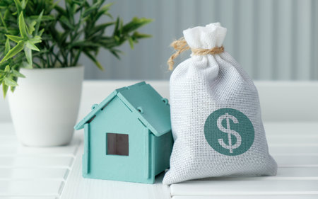 A house is next to a bag with a dollar sign on it. The house is blue. The bag is whiteの写真素材