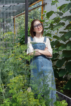 A woman in a blue dress stands in front of a plant. She is wearing glasses and has her arms crossedの写真素材
