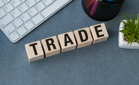 A keyboard is on a table with a potted plant. The letters TRADE are written on a wooden blockの写真素材