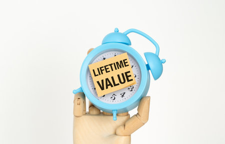A blue alarm clock with a note that says Lifetime Value. The clock is held by a person's handの写真素材