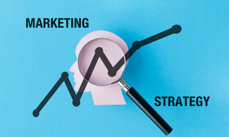 A magnifying glass is on a blue background with the words Marketing Strategy written below it. The...