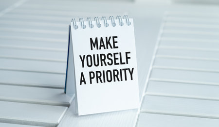 A white notebook with the words Make Yourself a Priority written on it. The notebook is sitting on a tableの写真素材