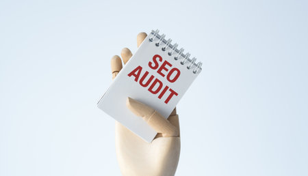 A hand holding a spiral notebook with the word SEO Audit written on it. The notebook is red and whiteの写真素材