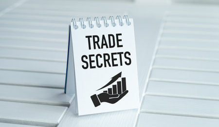 A white notebook with a hand holding a pen and the words Trade Secrets written on it. The notebook is on a tableの写真素材