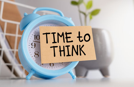 A blue alarm clock with a white face and a piece of paper with the words Time to Think written on itの写真素材