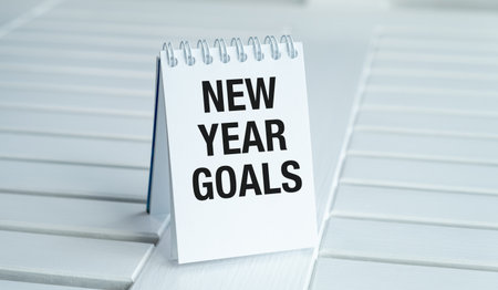 A white spiral bound notebook with the words New Year Goals written on it. The notebook is sitting on a tableの写真素材