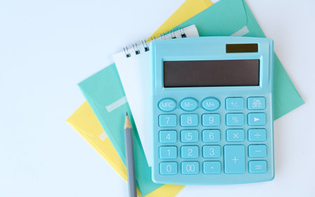 A blue calculator sits on top of a yellow envelope and a pencil. The calculator is on a white surfaceの写真素材