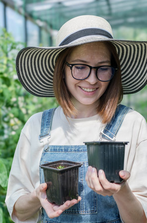 A woman wearing a straw hat and blue overalls holding two potted plants. She is smilingの写真素材