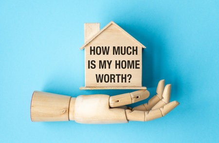 A wooden hand holding a house and the words How Much is my Home Worth written below itの写真素材