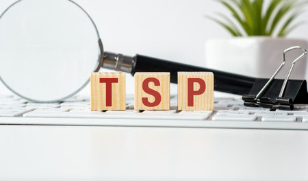 A magnifying glass is on a table with a keyboard and a stack of wooden blocks. The blocks spell out the word TPS on the keyboardの写真素材