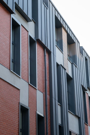 A brick building with a black roof. The building has a lot of windows. The windows are rectangular and are of different sizesの写真素材