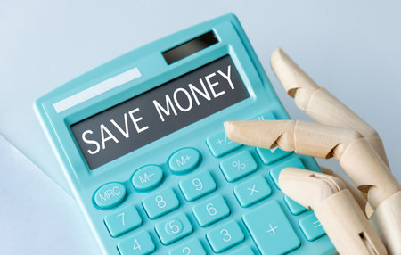 A calculator with the word Save Money on it. A hand is pressing the calculatorの写真素材
