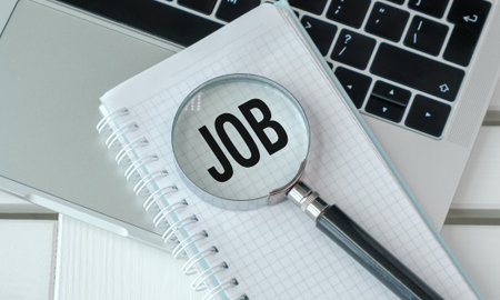 A magnifying glass is on top of a notebook with the word Job written on it. The magnifying glass is black and silverの写真素材