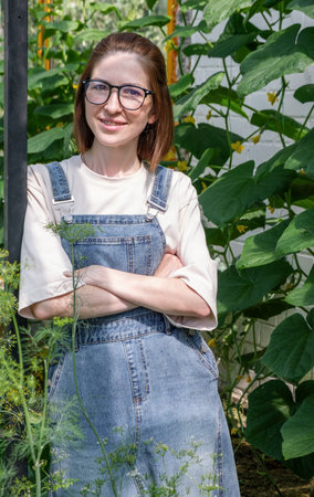 A woman in a denim overalls is standing in front of a plant. She is wearing glasses and a white shirtの写真素材