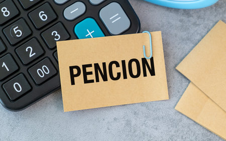 A calculator is placed on a table with a piece of paper that says PENCION on it. The paper is attached to the calculator with a paper clipの写真素材