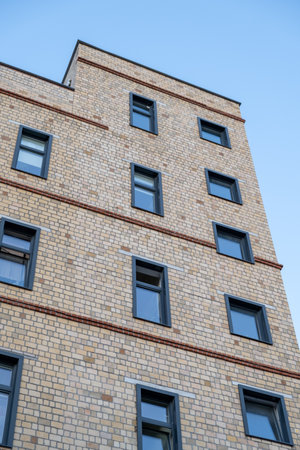 A tall brick building with many windows. The windows are black and the building is brown. The sky is blueの写真素材