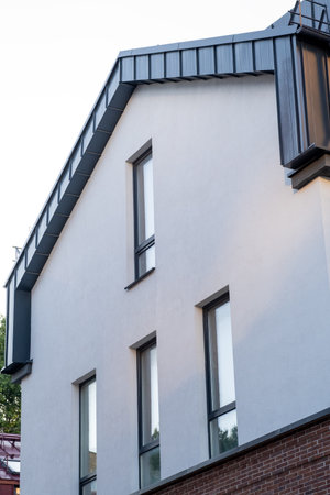 A building with a slanted roof and a window on the side. The window is on the side of the building and is facing the street. The building is made of bricks and has a grey colorの写真素材