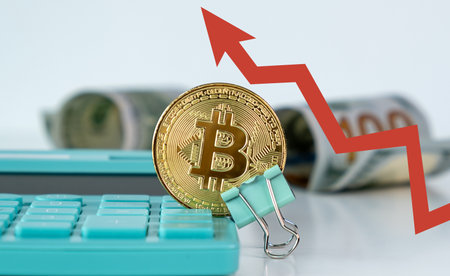 A calculator with a coin on it and a red line. The calculator is blue. The coin is a Bitcoinの写真素材