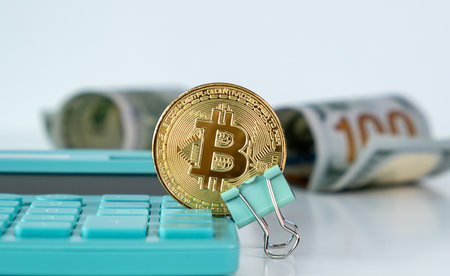 A calculator with a coin on it and a stack of bills. The coin is a B and the calculator is blueの写真素材