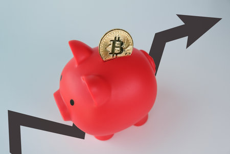 A red piggy bank with a gold coin inside. The coin is labeled with the letter Bitcoinの写真素材