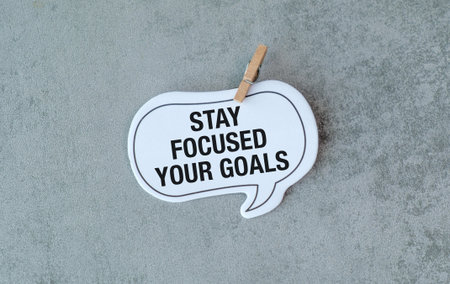 A white sign that says Stay focused on your Goals. It is hanging on a wall. The sign is attached to...