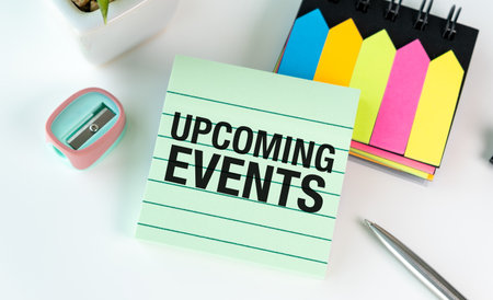 A green sticky note with the word Upcoming Events written on it. The note is on top of a stack of...