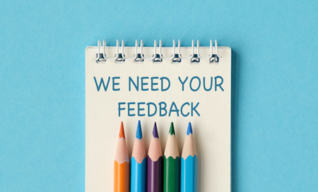 A notebook with pencils on it that says We need your feedback. The pencils are in different colors