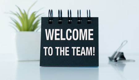 A black notebook with the words Welcome to the Team written on it. The notebook is on a table with a potted plant in the backgroundの写真素材